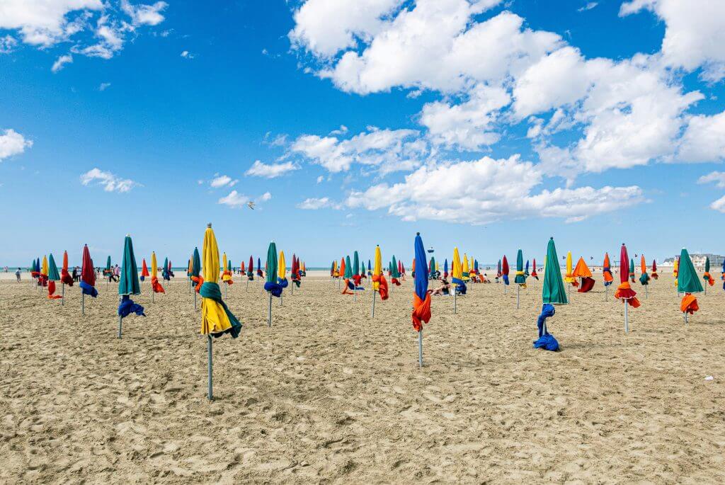 Plage la Côte fleurie de Deauville avec ses célèbres parasols colorés - Photo de <a href="https://unsplash.com/fr/@tom2185?utm_content=creditCopyText&utm_medium=referral&utm_source=unsplash">Tom Delanoue</a> sur <a href="https://unsplash.com/fr/photos/un-tas-de-parapluies-qui-sont-dans-le-sable-y5K607TThzU?utm_content=creditCopyText&utm_medium=referral&utm_source=unsplash">Unsplash</a>